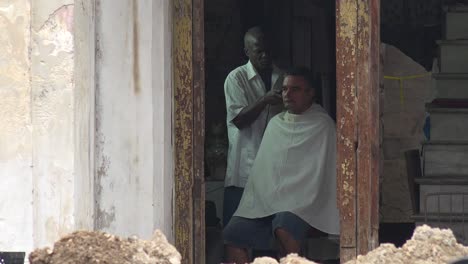 a customer gets a haircut along a primitive street in havana cuba