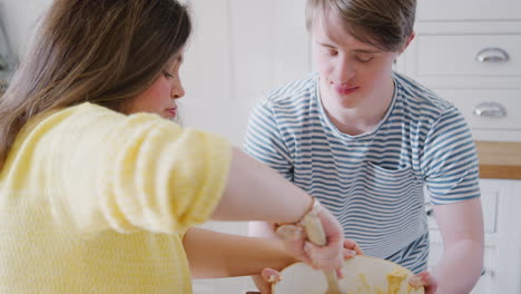 una pareja joven con síndrome de down mezcla ingredientes para una receta de pastel que están horneando en la cocina en casa.
