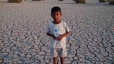 child standing in parched landscape, clutching water bottle, symbolizing devastating drought impacts and global climate crisis affecting vulnerable populations