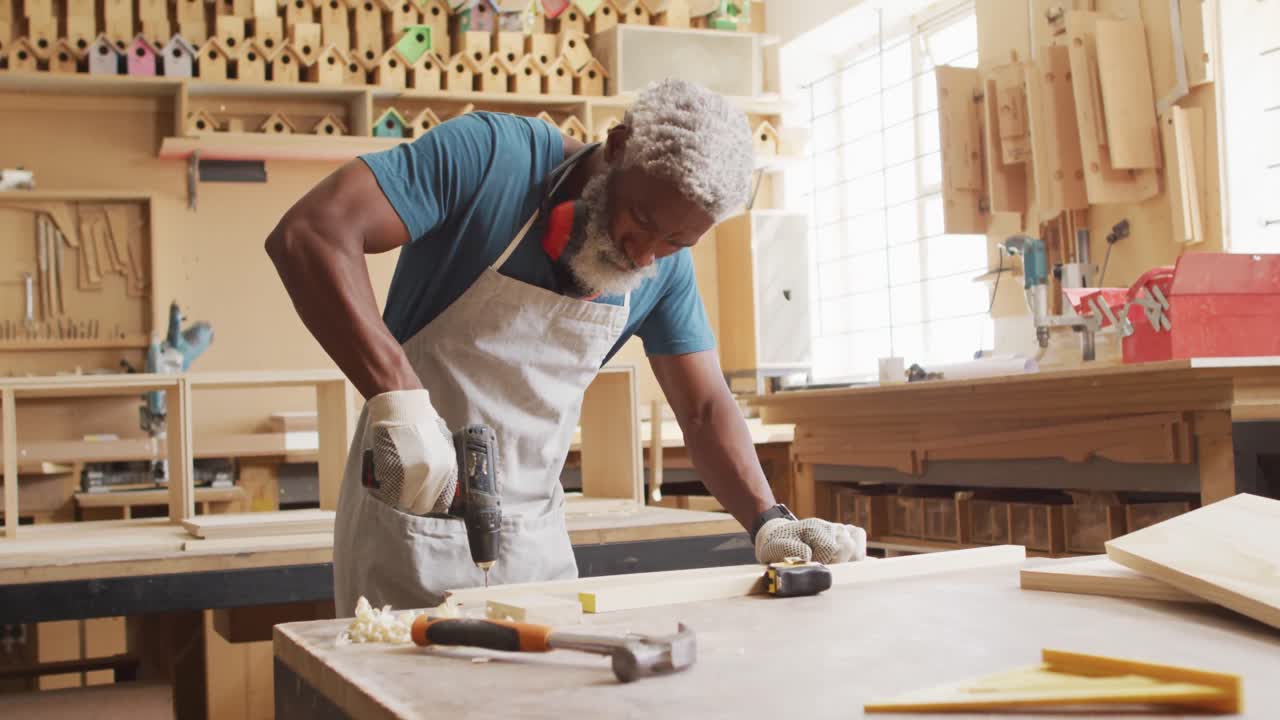 carpintero afroamericano perforando agujeros en una tabla de madera usando una máquina de perforación manual