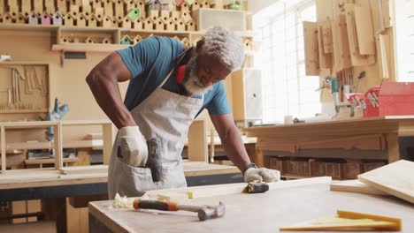 carpintero afroamericano perforando agujeros en una tabla de madera usando una máquina de perforación manual