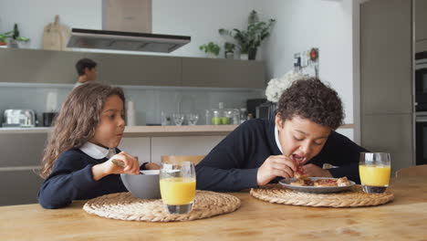 Kinder-Frühstücken-Vor-Der-Schule,-Während-Sich-Die-Eltern-Für-Die-Arbeit-In-Der-Küche-Vorbereiten