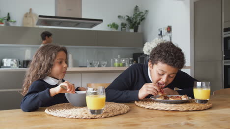 children eating breakfast before school as parents get ready for work in kitchen