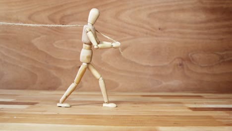 Wooden-figurine-pulling-a-rope-on-wooden-floor