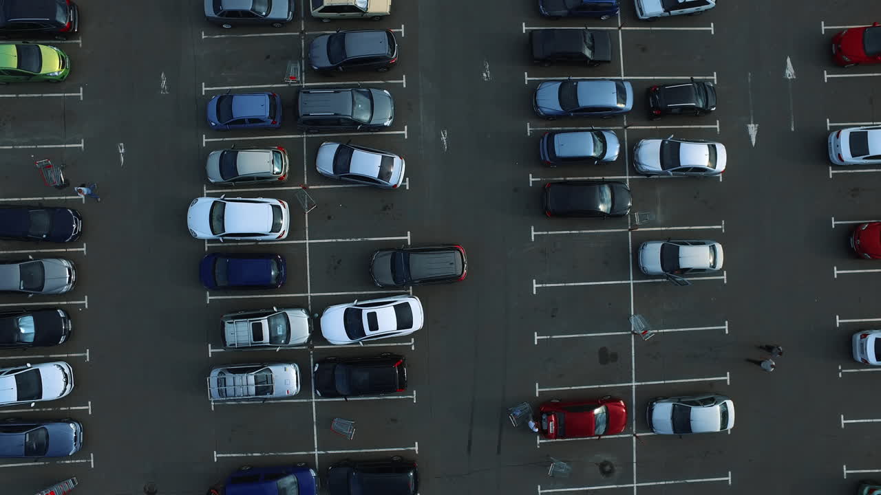 Droneopptak av biler som parkerer på overfylte parkeringsplasser. Folk går på parkeringsplassen.