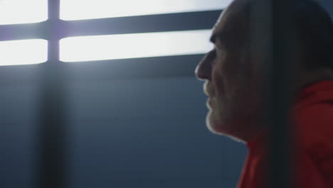 Close-Up-of-Prisoner-in-Orange-Uniform-Holding-Metal-Bars-in-Prison-Cell----------(Stock-Footage)