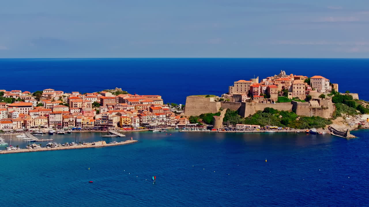 Aerial drone shot over the coastal town of Calvi in Corsica. View of the citadel fortress overlooking the city. Summer holidays destination. Bright blue sky, vibrant turquoise sea