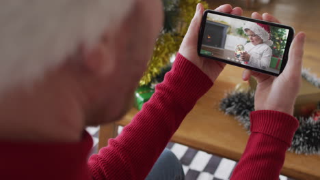 hombre caucásico con sombrero de santa usando un teléfono inteligente para una videollamada de navidad con un niño sonriente en la pantalla