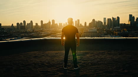 man standing on rooftop overlooking city at sunset