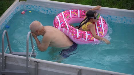 el abuelo con la nieta se divierten en la piscina. el abuelo juega con el niño. la familia disfruta de las vacaciones de verano en una piscina saltando, girando, salpicando agua.