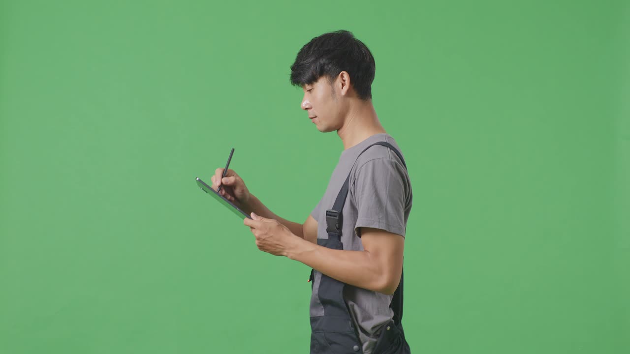 녹색 스크린 배경 스튜디오에서 는 동안 태블릿에 메모를 취하는 아시아 남성 노동자의 측면 시각
