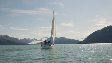 cruising sailboat on a calm sea amidst a beautiful mountain view of alaska usa -panning aerial shot