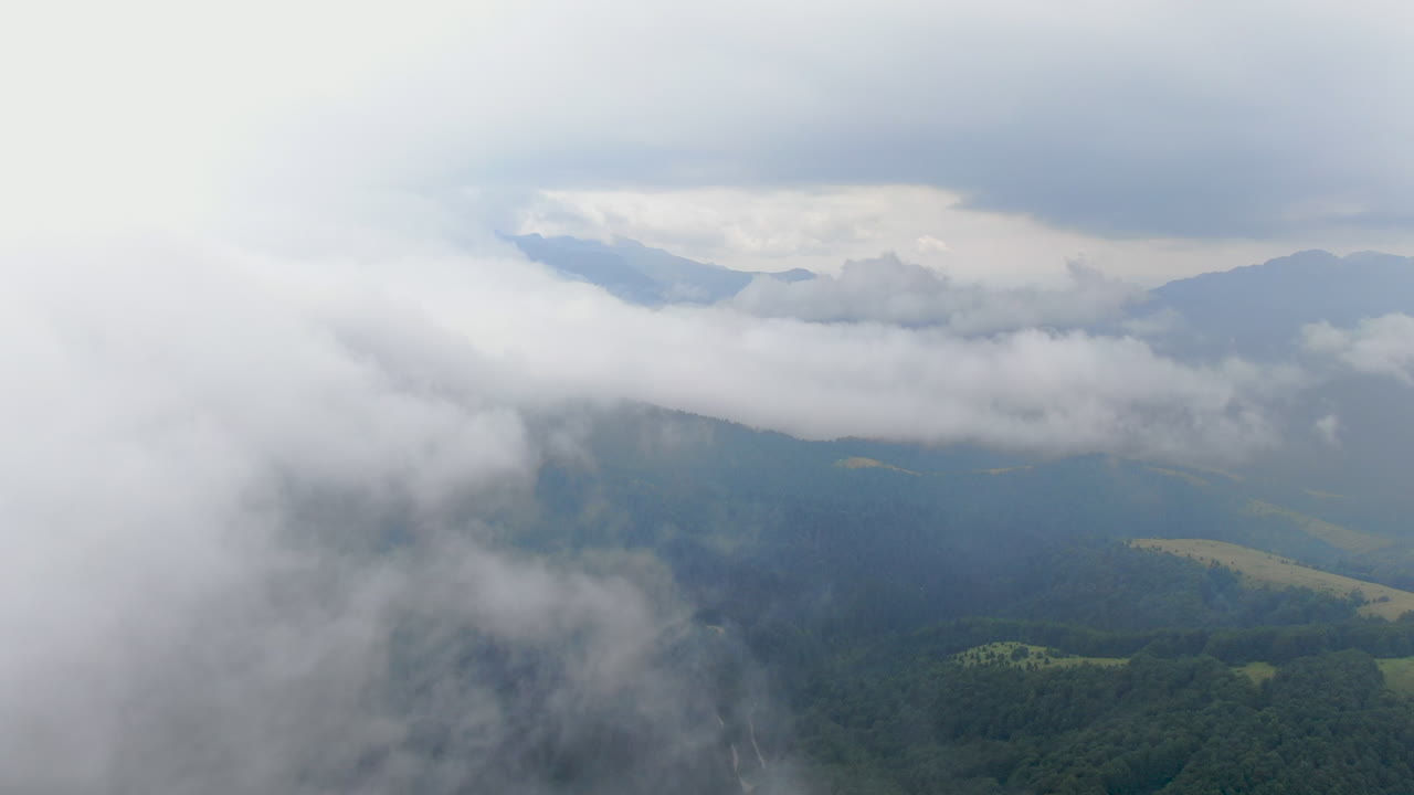 A landscape features mountains trees and a heavy cloud cover The light is subdued creating a misty atmosphere over the terrain