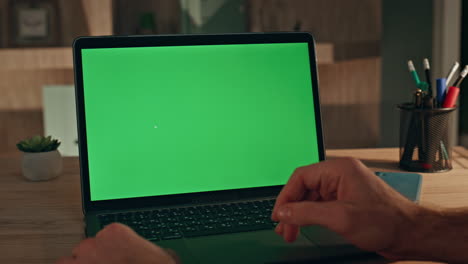 freelancer swiping touchpad chroma key laptop at evening workplace close up.