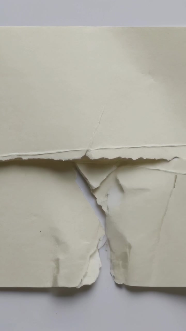 Vertical video: Beige sheet tearing from small rip on white surface revealing triangular flap