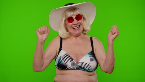 Mature-old-woman-traveler-in-red-sunglasses-and-hat-dancing,-celebrating,-smiling-on-chroma-key