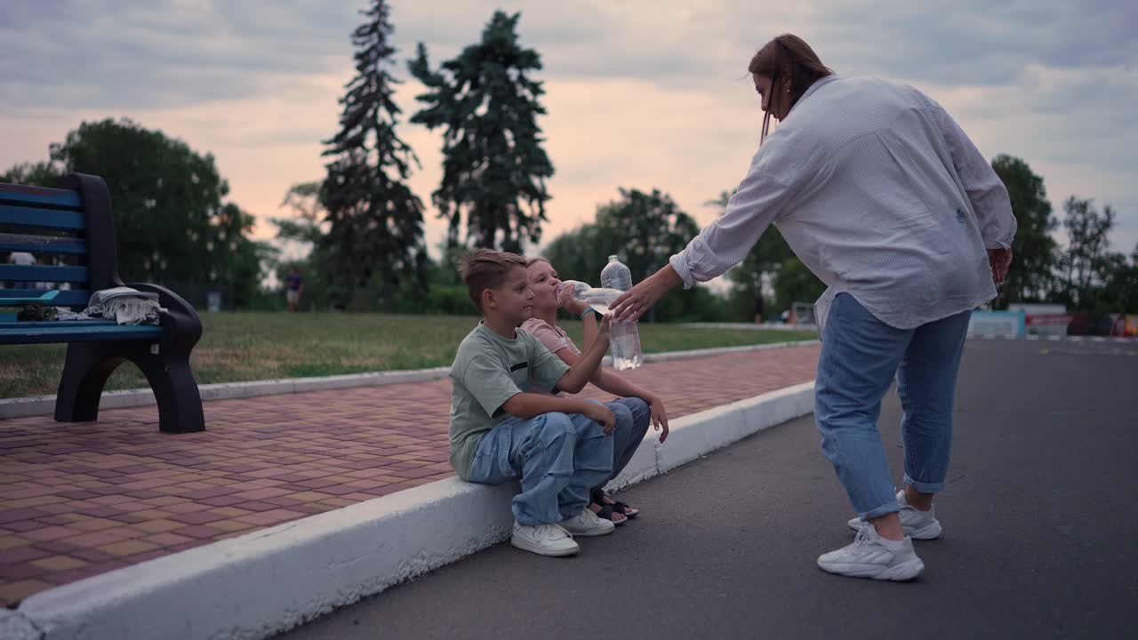 madre dando agua a los niños en un parque