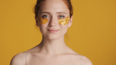 una chica pelirroja frente a la cámara sobre un fondo amarillo.