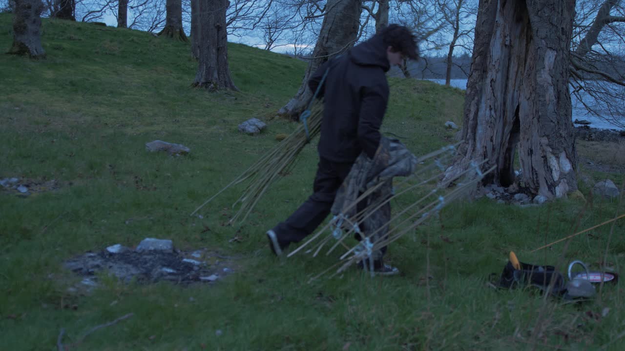 Young man camp site on island carrying supplies puts down makeshift fish trap