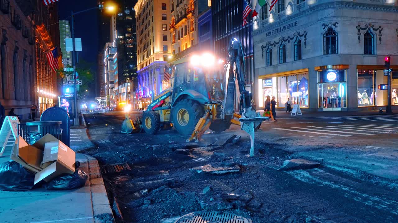 New York, USA, 5 oktober 2025: John Deere grävlastare gräver upp vägytan på natten. Tung maskin grävlastare gräver upp asfalt under nattligt vägarbete på Fifth Avenue på Manhattan.