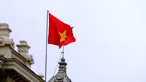 hanoi opera house rooftop with the vietnamese flag waving in slow motion, square of august revolution, zoomed in shot