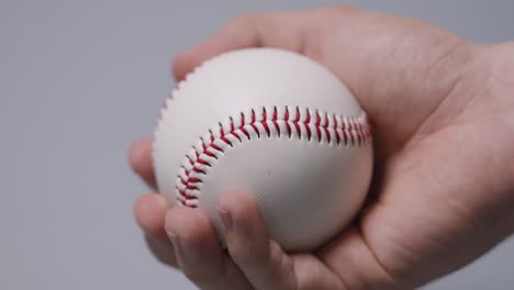 close up shot of hand holding baseball ball against grey background