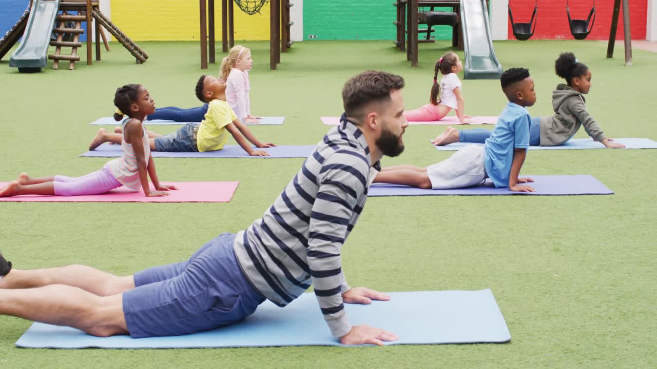 un maestro masculino diverso y escolares felices haciendo ejercicio en esteras en el patio de recreo de la escuela