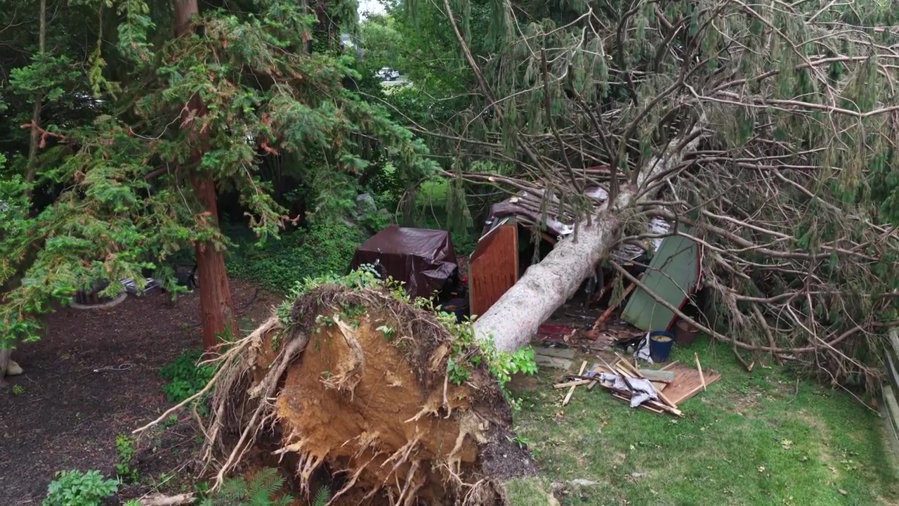 Enorme boomwortelkluit scheurt uit de grond nabij verpulverd schuurpuin in Manheim Township, Pennsylvania. Een achtertuin vuurplaats en volwassen bomen grenzen aan een door storm beschadigd bosrijk gazon. Luchtfoto met drone.