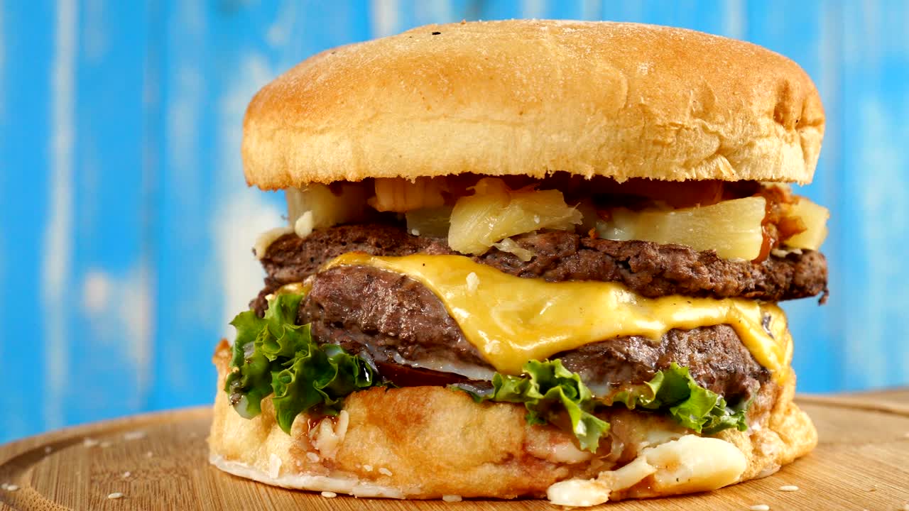 Burger, with a beef, cheese, and vegetables rotates on a wooden Board. On blue wooden background