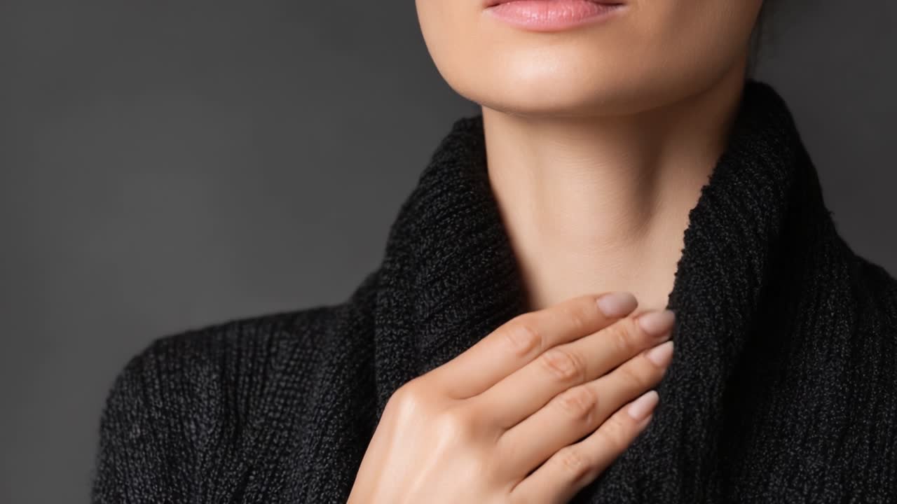 Ritratto accattivante di una donna con un gesto aggraziato, che enfatizza eleganza e compostezza mentre mostra il suo elegante capo in maglia su uno sfondo neutro.