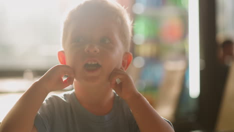 little boy with open mouth closes ears by fingers in room