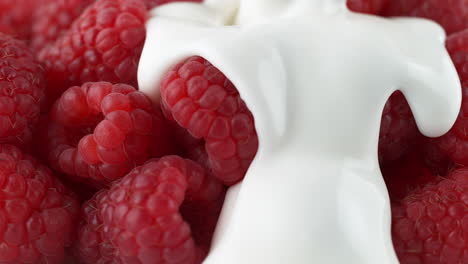verter yogur sobre frambuesas maduras - una fruta cubierta de líquido que se enrolla hacia abajo