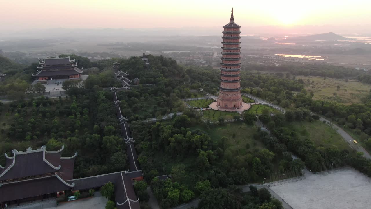 vista aérea de drones en vietnam volando sobre una zona de templo budista y pagoda llena de árboles verdes frente al sol en ninh binh al atardecer