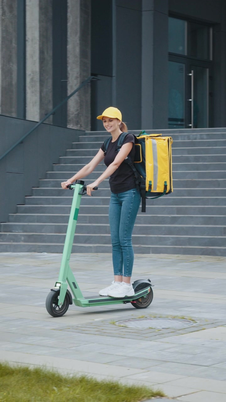 A delivery person smiles while riding an electric scooter with a food delivery backpack in a