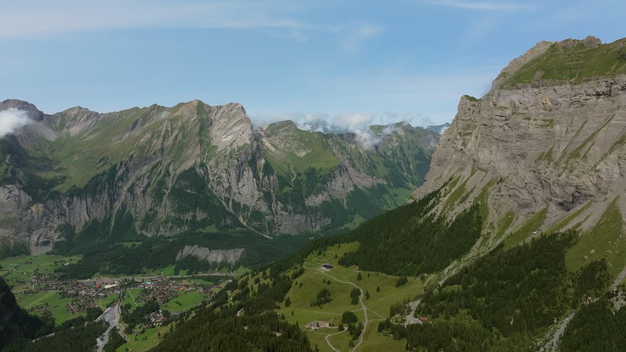 Drone aerial view of the Swiss Alps near Kandersteg, showing steep rocky cliffs, lush green slopes, and a picturesque alpine valley with the village below
