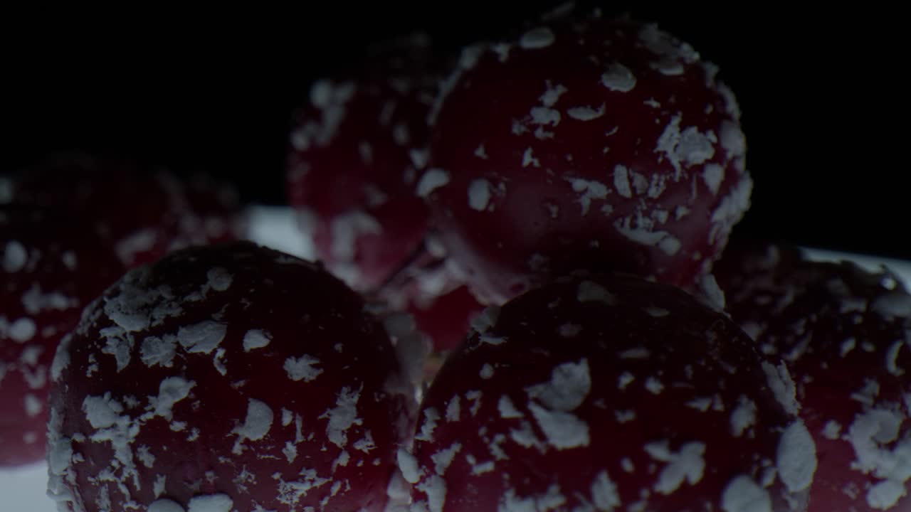 Macro close up of red spherical objects with white flakes slowly spinning in studio lighting creating an abstract texture pattern and visually engaging motion background