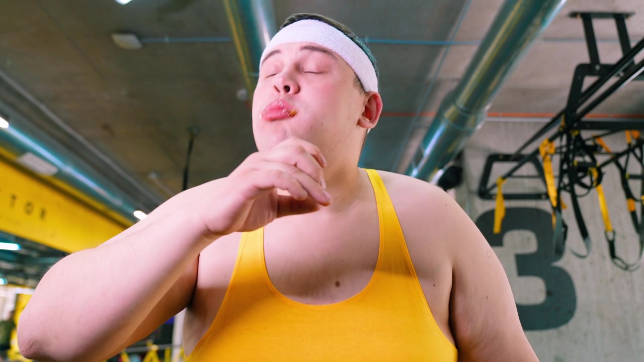 Overweight Man Eats a Burger in the Gym