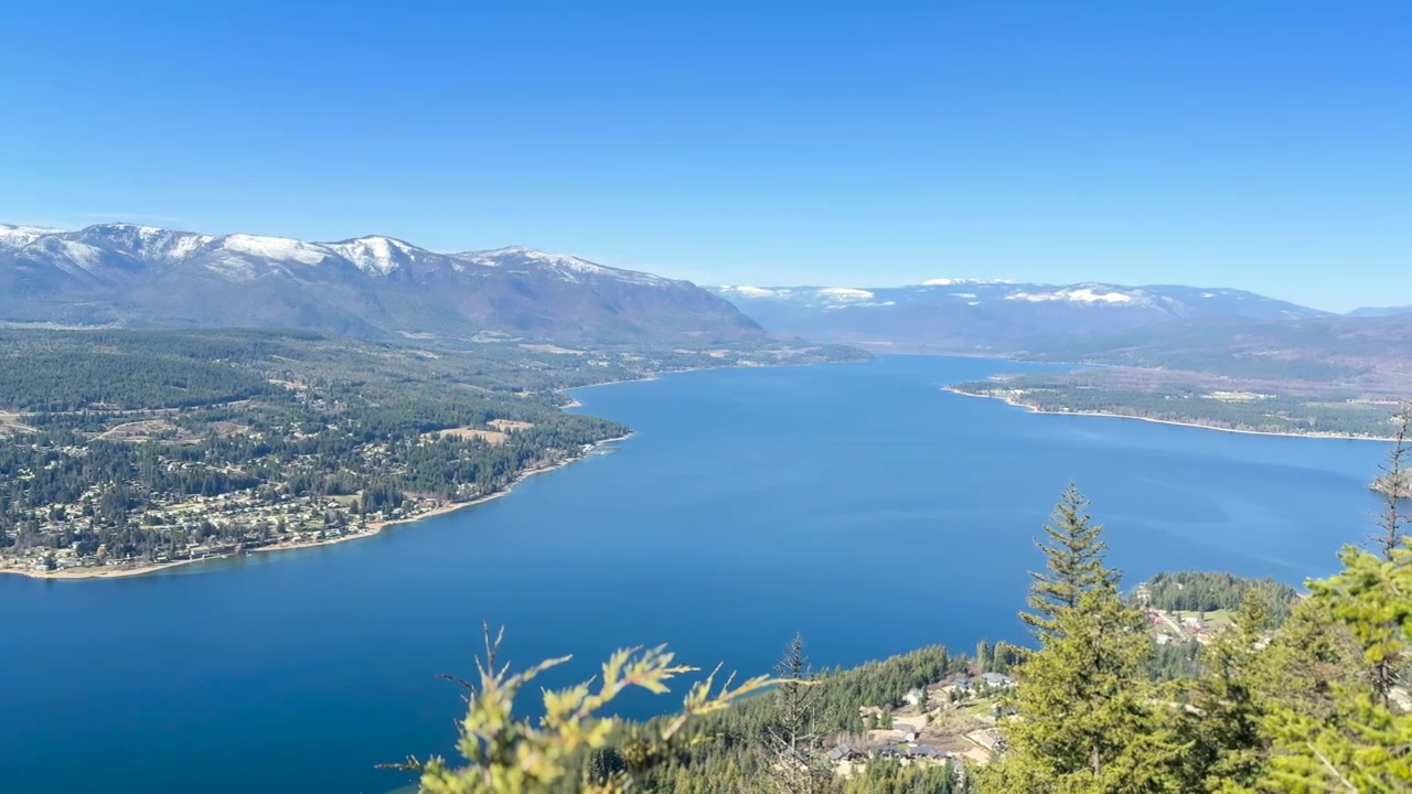 Scatto a mano libera di un lago sereno circondato da montagne innevate e vegetazione lussureggiante al lago Shuswap, Blind Bay, con illuminazione chiara ed equilibrata
