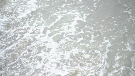 Waves-washing-small-rock-and-sand-with-daylight-reflection