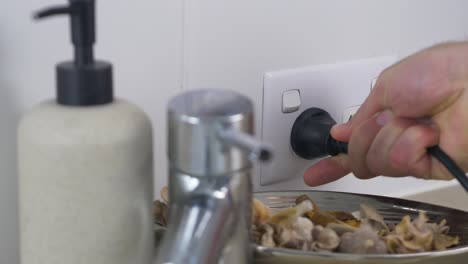 close-up slow motion shot of person plugging in power chord cable into socket wall electricity with tap and moisturiser soap dispenser bathroom personal hygiene 4k