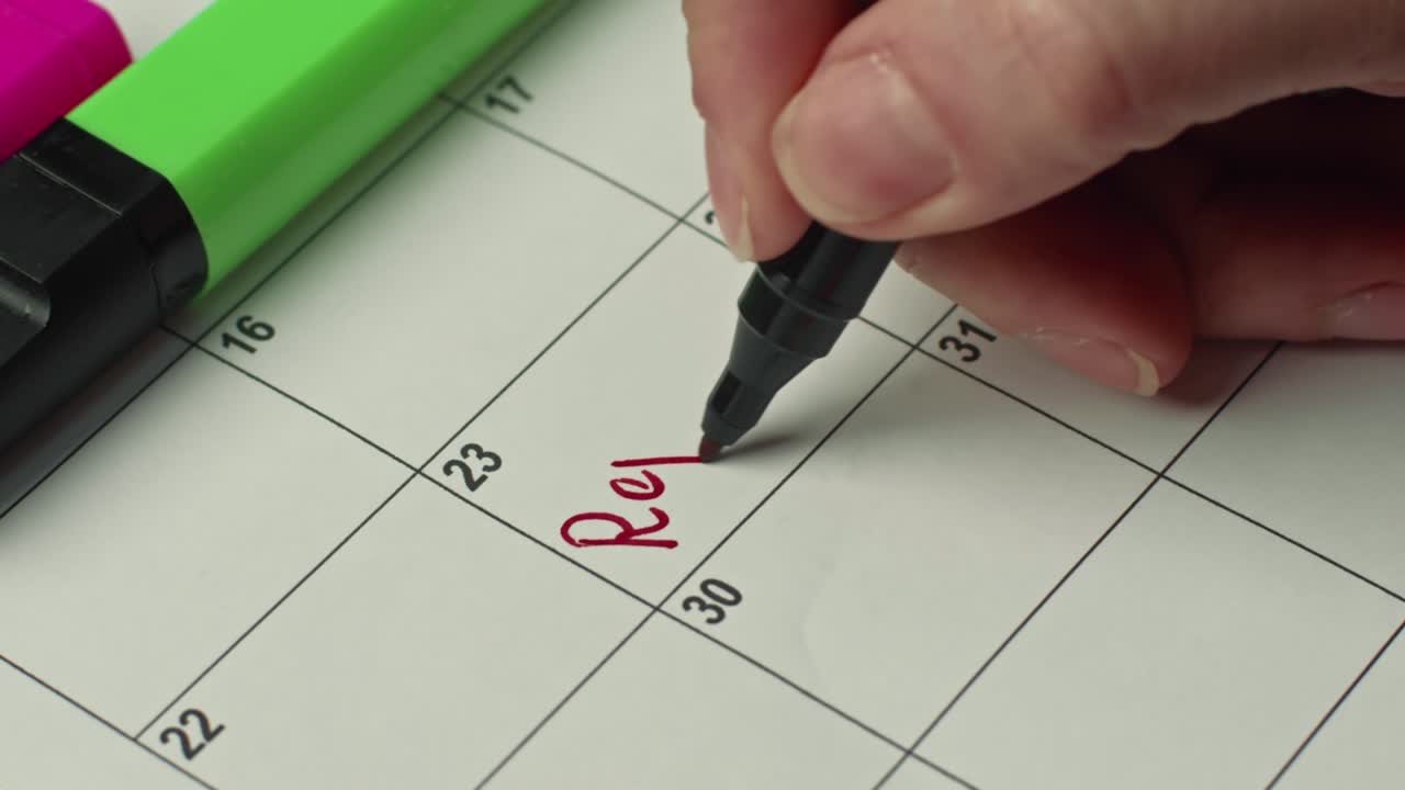 primer plano de un informe de recordatorio escrito a mano por una mujer con un marcador rojo en un calendario de papel