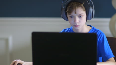 young teen boy with headphones on playing on a laptop