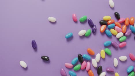 Video-of-overhead-view-of-multi-coloured-sweets-falling-over-purple-background