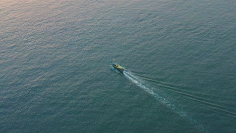 a colorful local fishing boat traveling through the tropical waters of bali during sunset, aerial follow