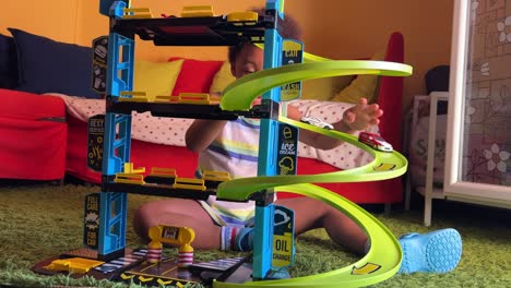 lovely 3-year-old black child amused playing with a toy garage at home over a green rug