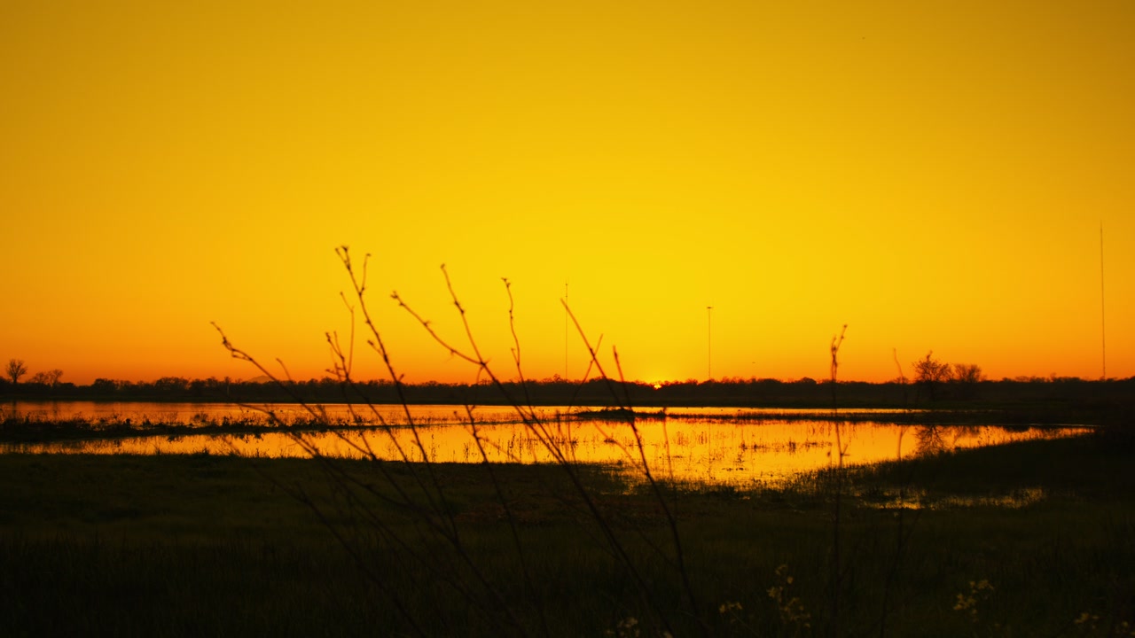 A smooth horizontal panning shot capturing a vibrant orange and yellow sunset over a calm lake.