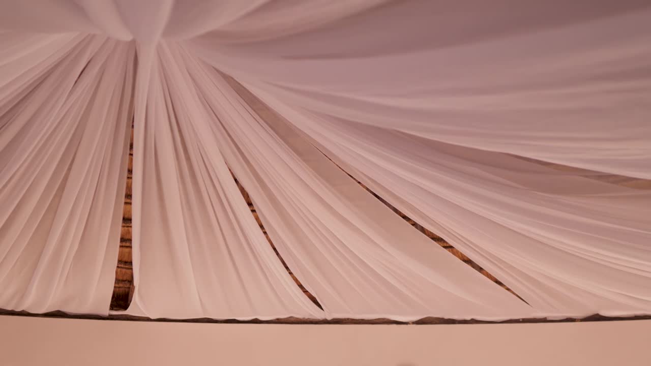 A roof of white fabrics drape down into a funnel. The fabrics blow in the wind.