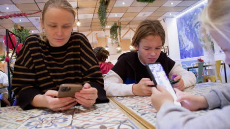 mamá y los niños están en sus teléfonos en un café - 1
