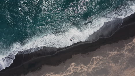 Aerial:-Top-down-shot-of-two-children-walking-on-Vlychada-beach-of-Santorini,-Greece