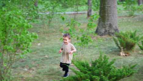 lovely baby boy walks among the green bushes and stones. happy kid runs by the grass in the park.